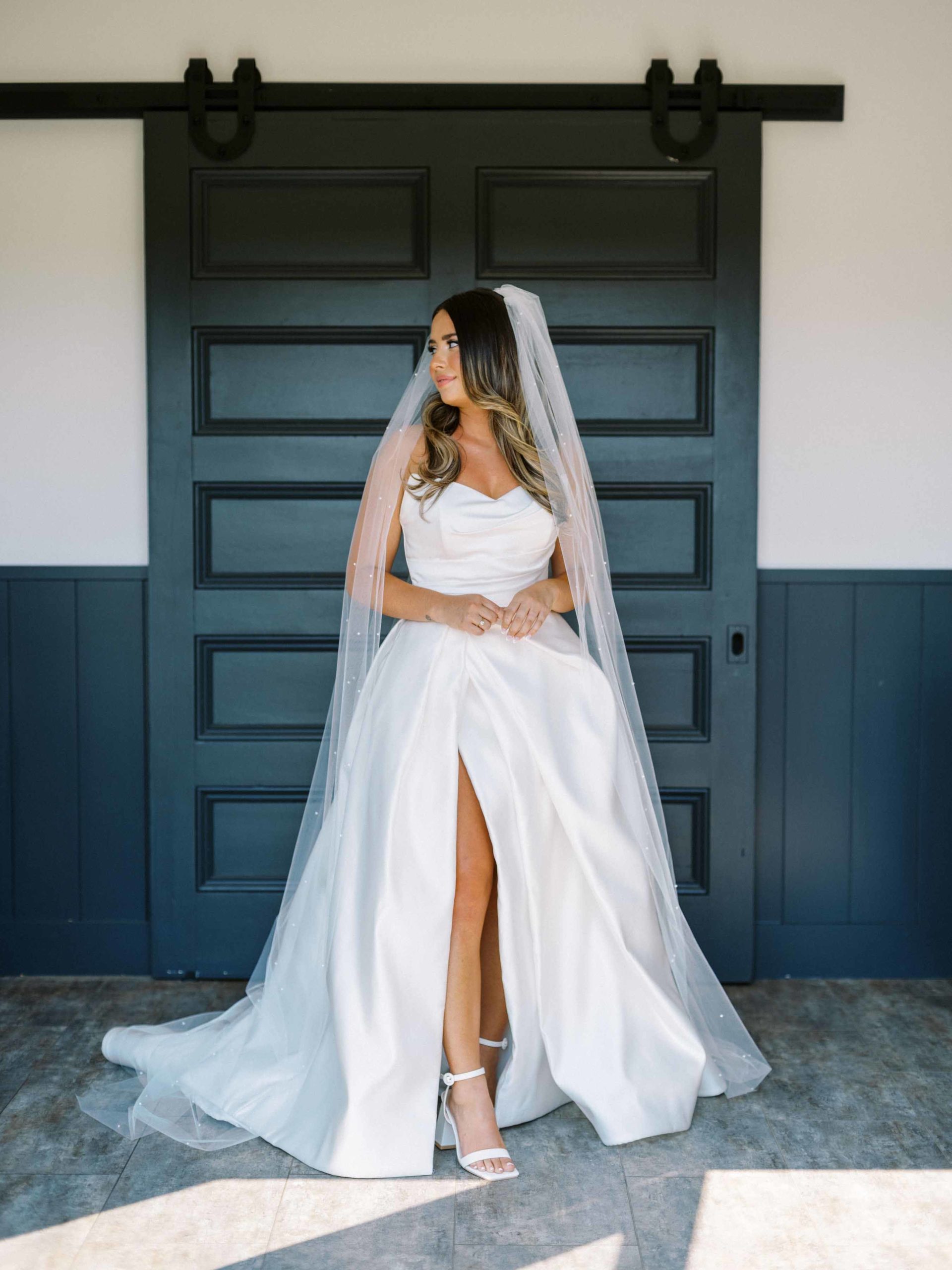 Hannah in wedding dress with slit in front of black doors